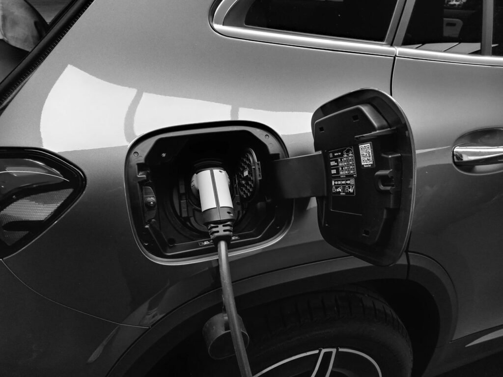 Close-up black and white image of an electric vehicle charging at a station.